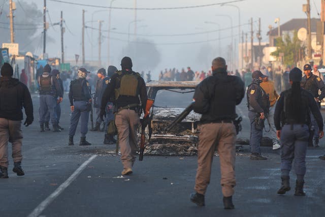 <p>Cape Town law enforcement officials stand around a burnt-out vehicle in Nyanga</p>